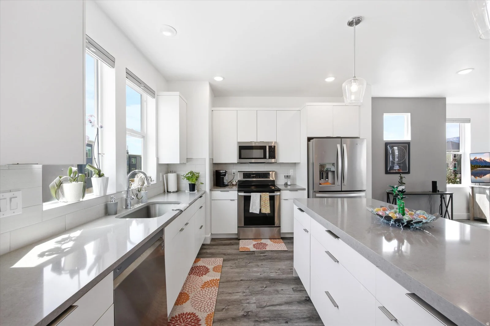 Kitchen featuring stainless steel appliances, white cabinets, light stone counters, hanging light fixtures, and dark wood-style flooring