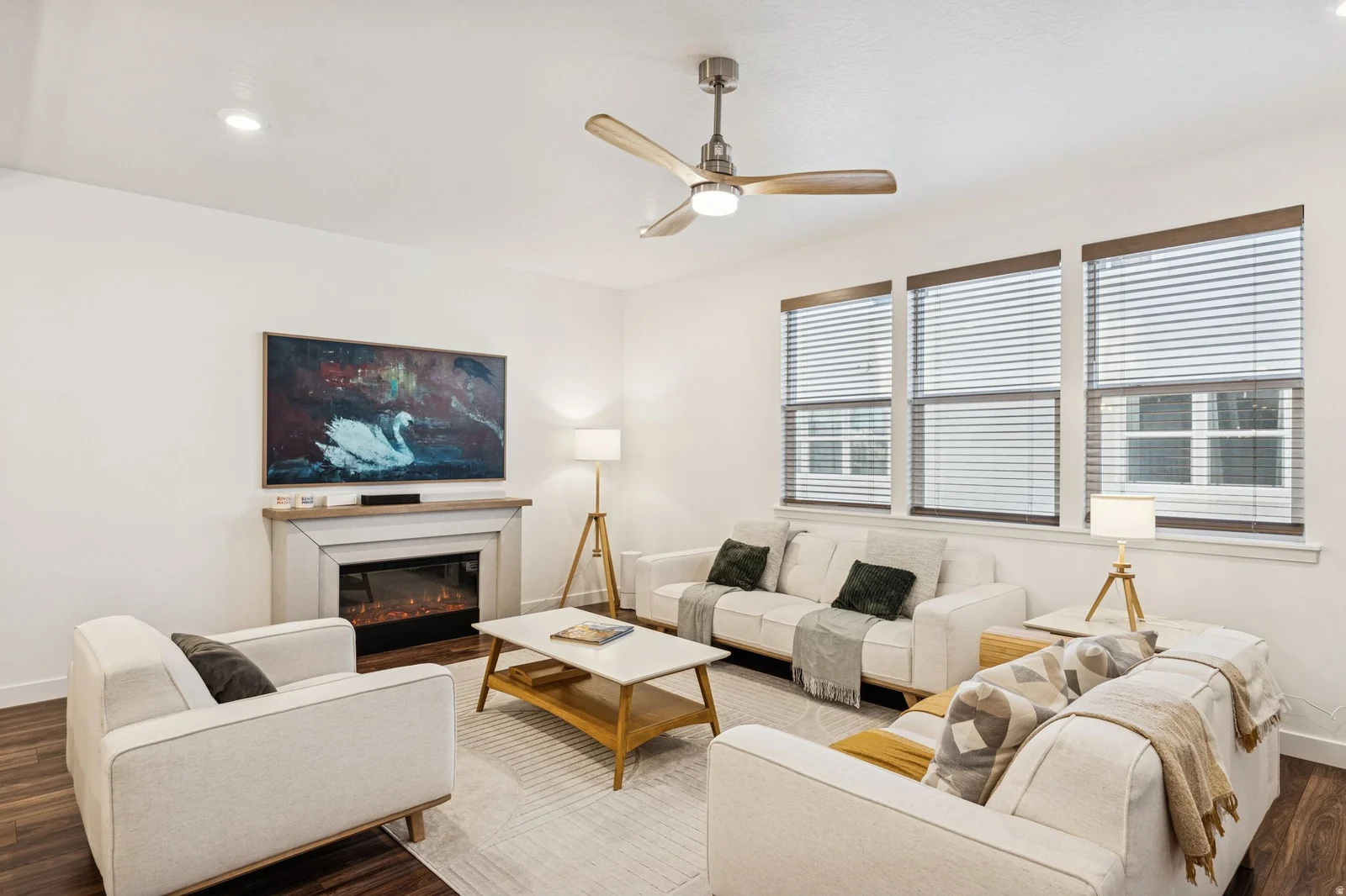 Living area featuring wood-finish flooring, a contemporary fireplace with a light-toned mantel, recessed lighting, and multiple windows with blinds