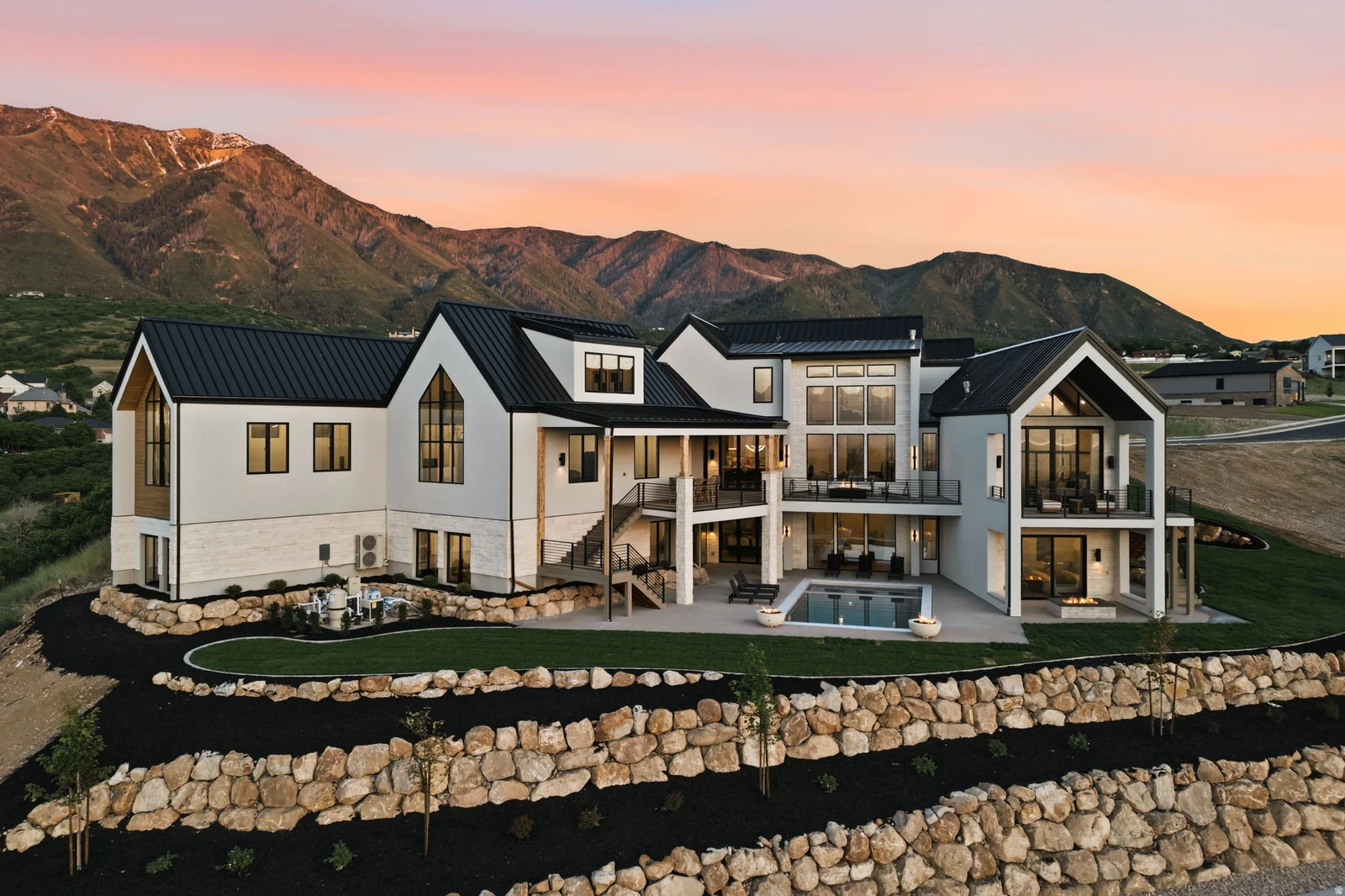 Contemporary architectural design featuring expansive glass, multiple balconies, a lower-level patio with a swimming pool, and tiered landscaping