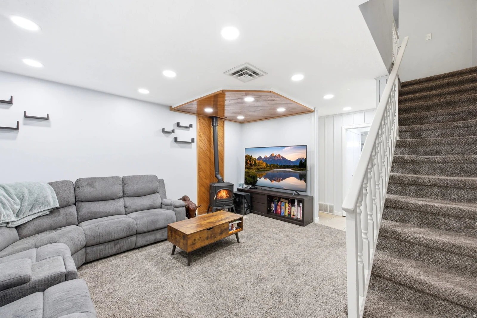 Carpeted living area featuring a wood-burning stove with a metal flue, recessed lighting, and a wood-paneled ceiling accent