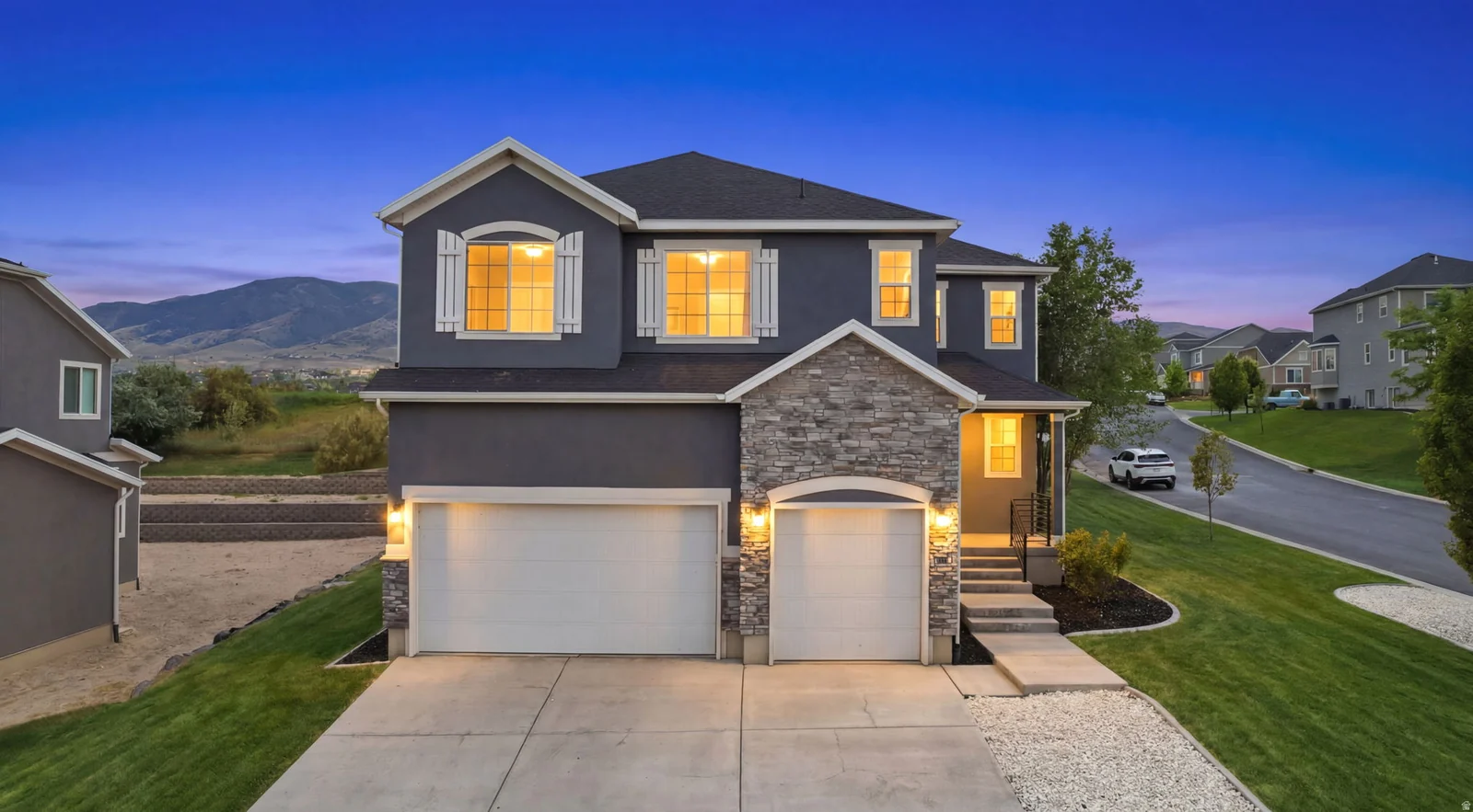 Two-story residence featuring a gray stucco exterior with stone accents, a two-car garage, and white window shutters