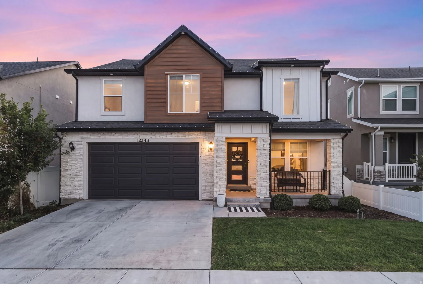 Contemporary facade featuring a dark gray garage door, stacked stone accents, and a covered porch