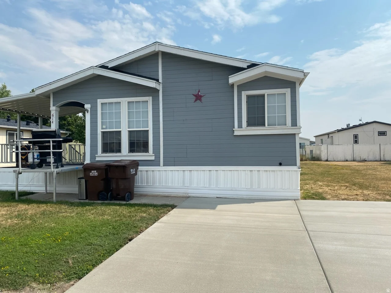 Manufactured home featuring blue siding with white trim, a covered porch, and a freshly repaired concrete driveway