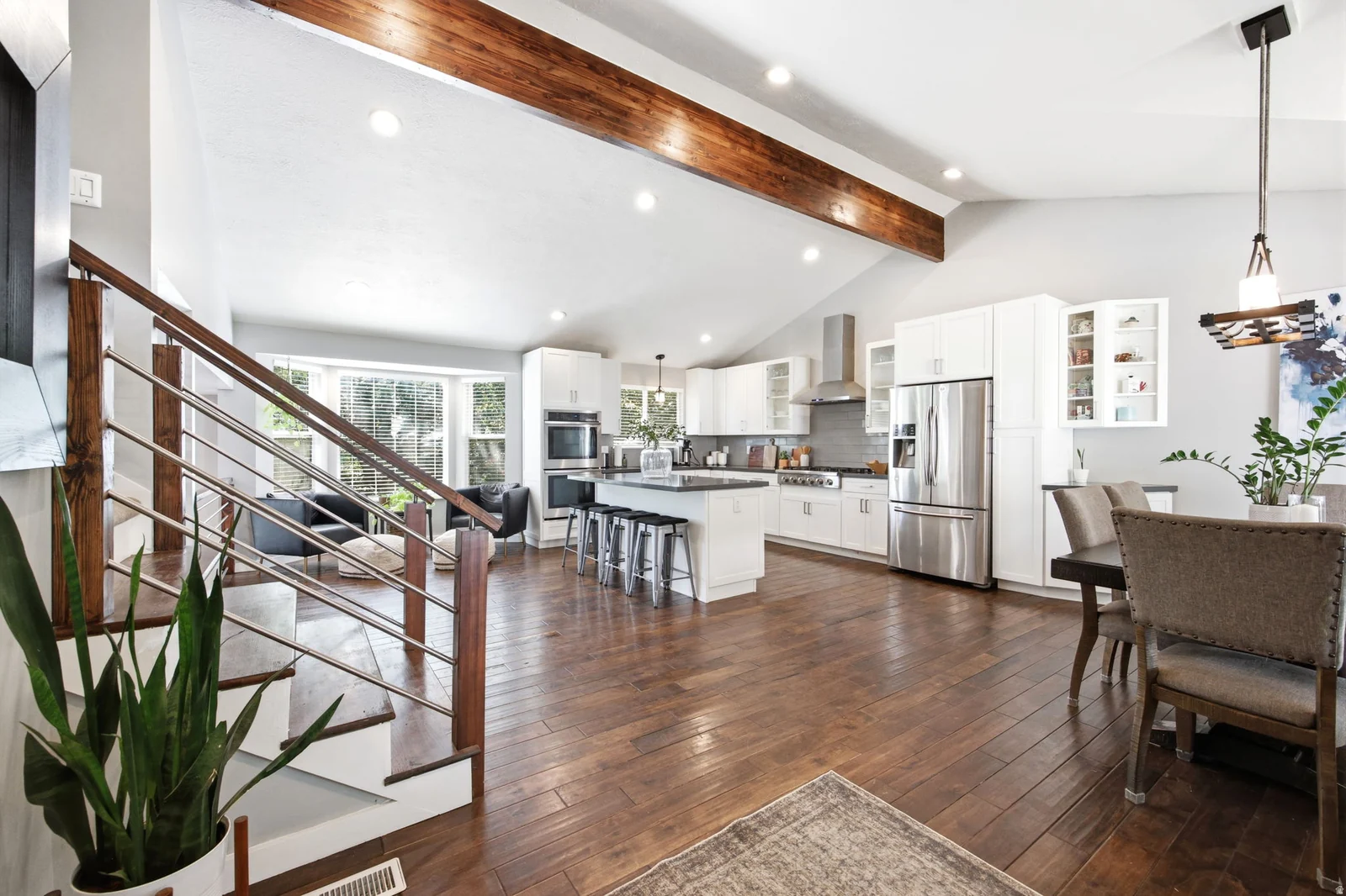 Open-concept interior featuring vaulted ceilings with exposed wood beams, wood-finish flooring, and a modern staircase with wood and metal railings