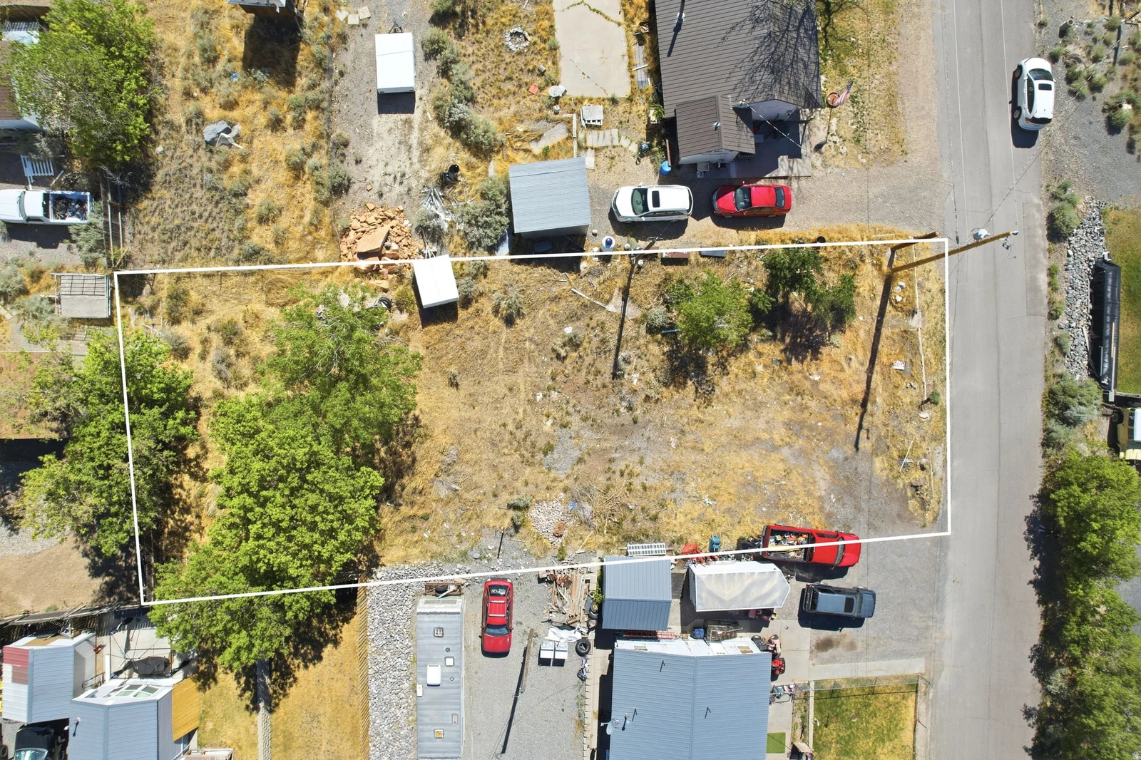 Vacant land parcel featuring mature trees, a clear boundary outline, direct street access, and surrounding established properties