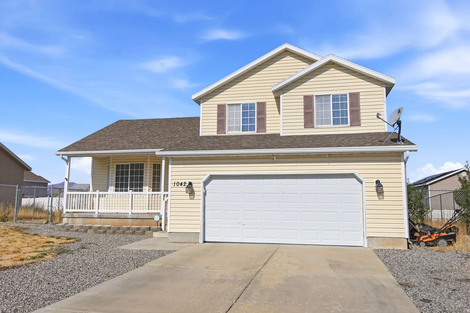 Two-story residence featuring light-colored siding, a covered front porch, an attached garage, and contrasting brown window shutters