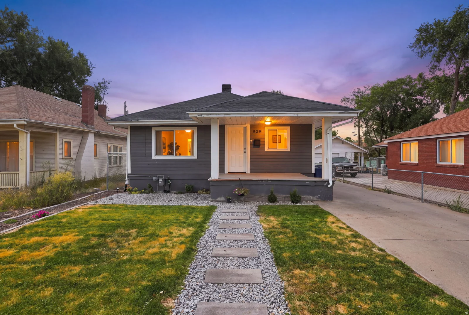 Charcoal gray exterior siding with white trim, dark shingle roof, covered front porch, concrete driveway, and a gravel and paver front walkway
