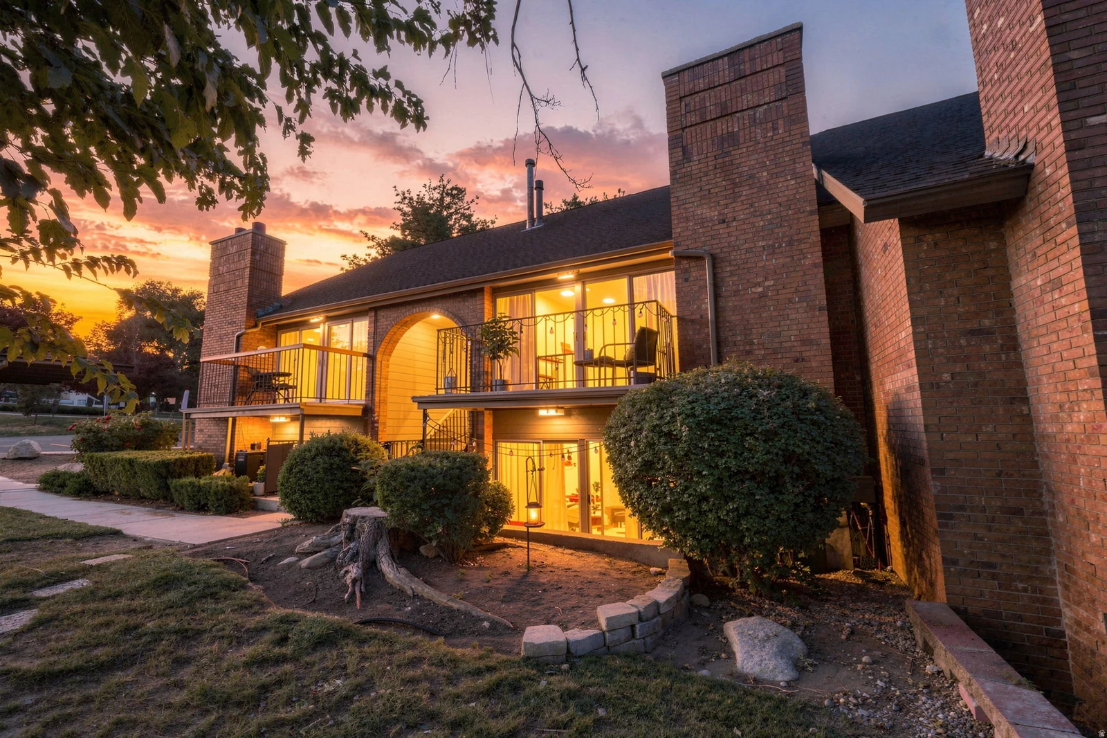 Brick exterior with multiple balconies, arched entryway, and mature landscaping