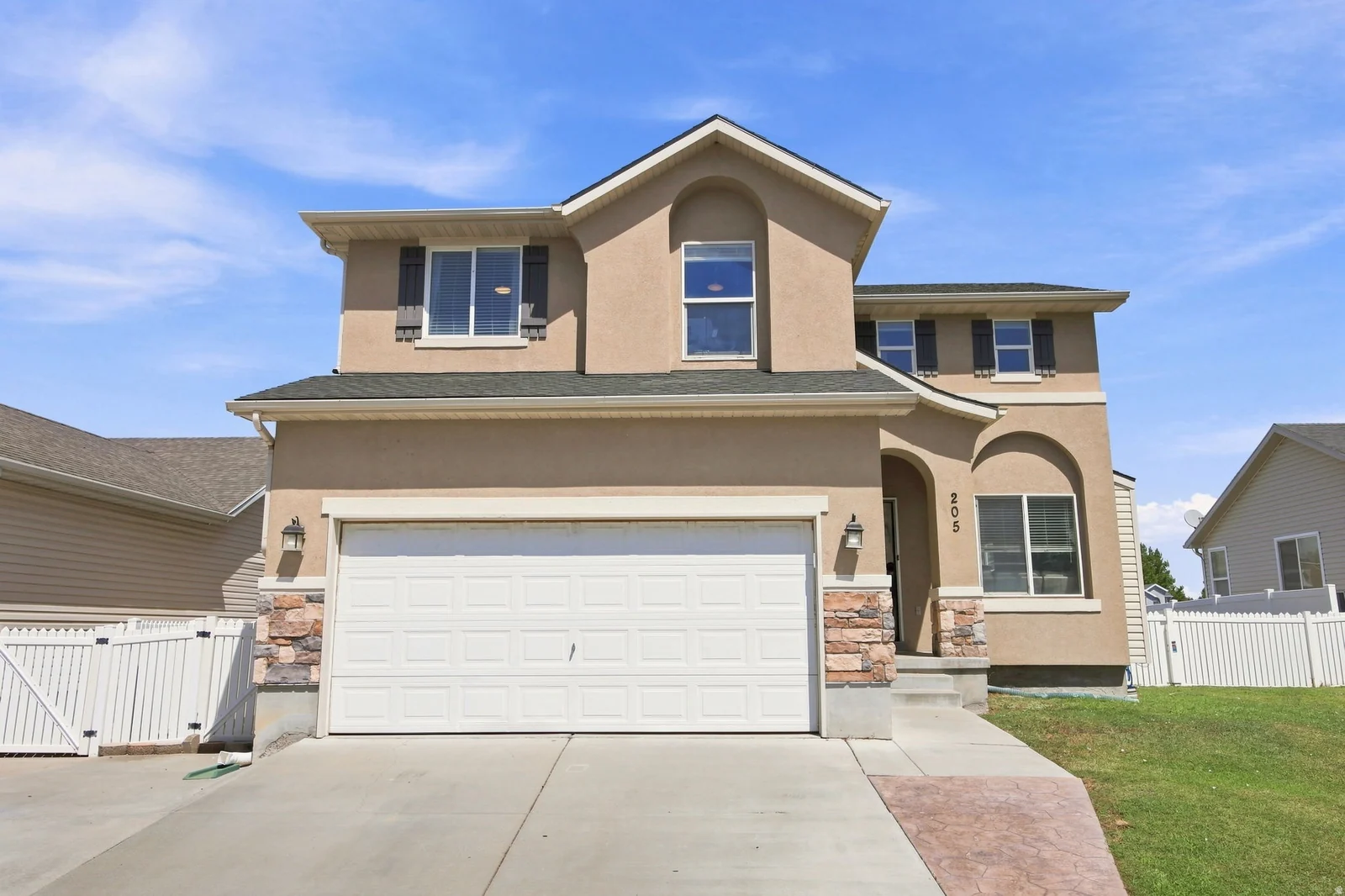 Stucco exterior with stone accents, attached two-car garage, concrete driveway, and white picket fencing