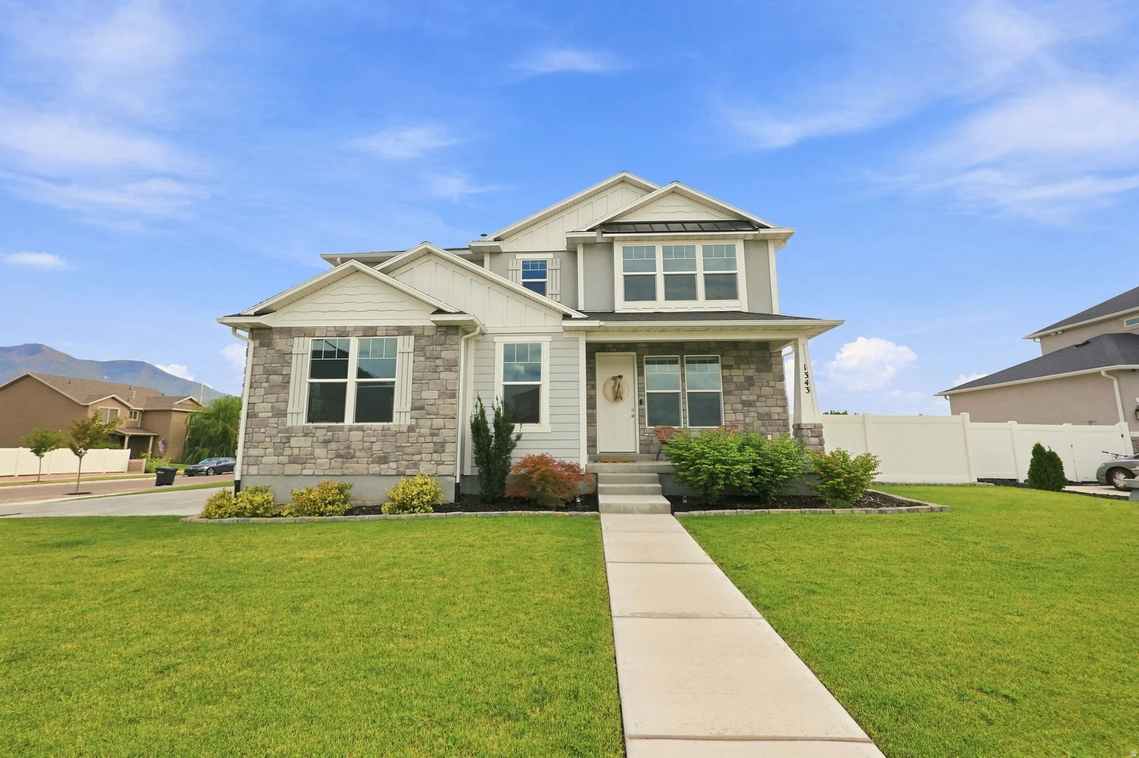 Two-story residence featuring a stone and siding facade, a covered front porch, and mature front yard landscaping