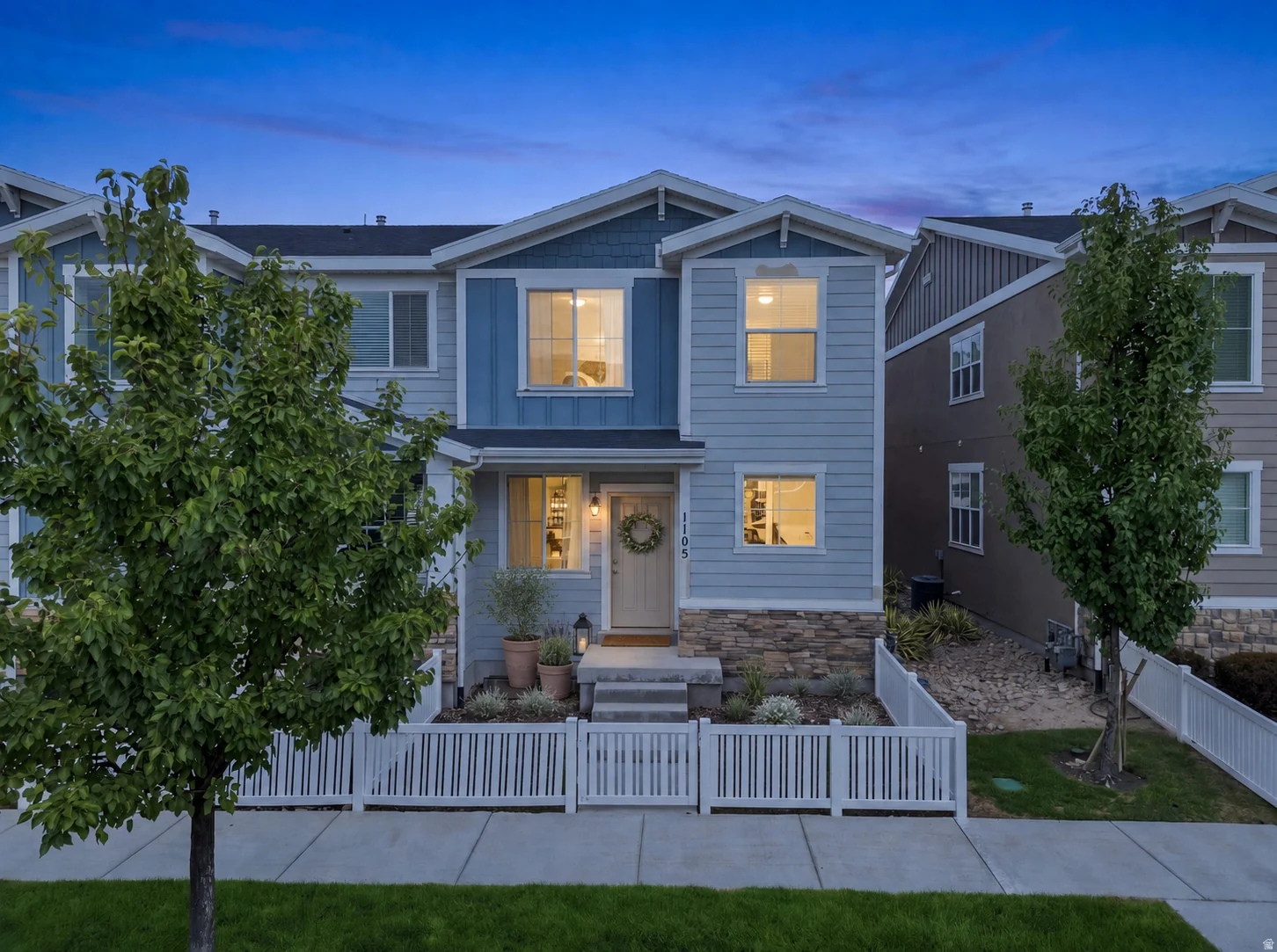 Two-story residence featuring light blue siding, stone facade accents, a white picket fence, and concrete steps leading to the front entry