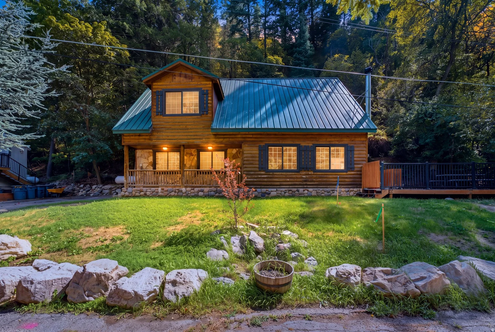 Log cabin exterior with a green metal roof, a covered front porch, and a side deck