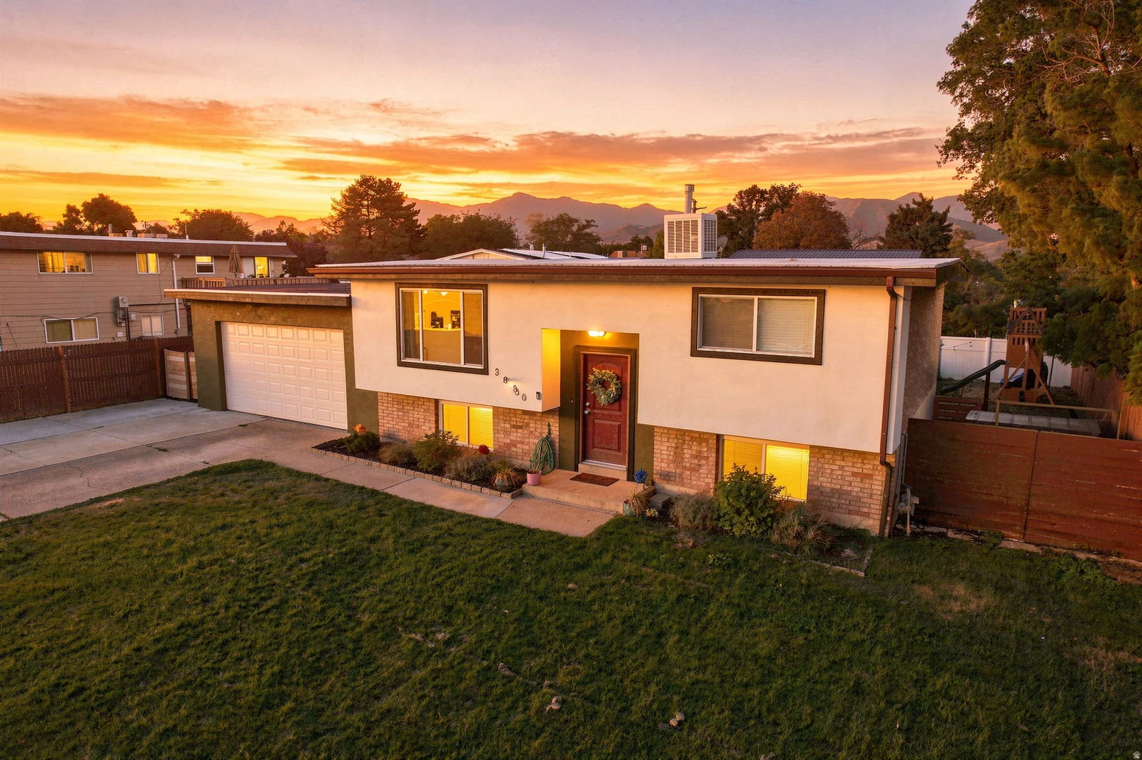 Split-level residence featuring a two-car garage, front lawn, and mature trees
