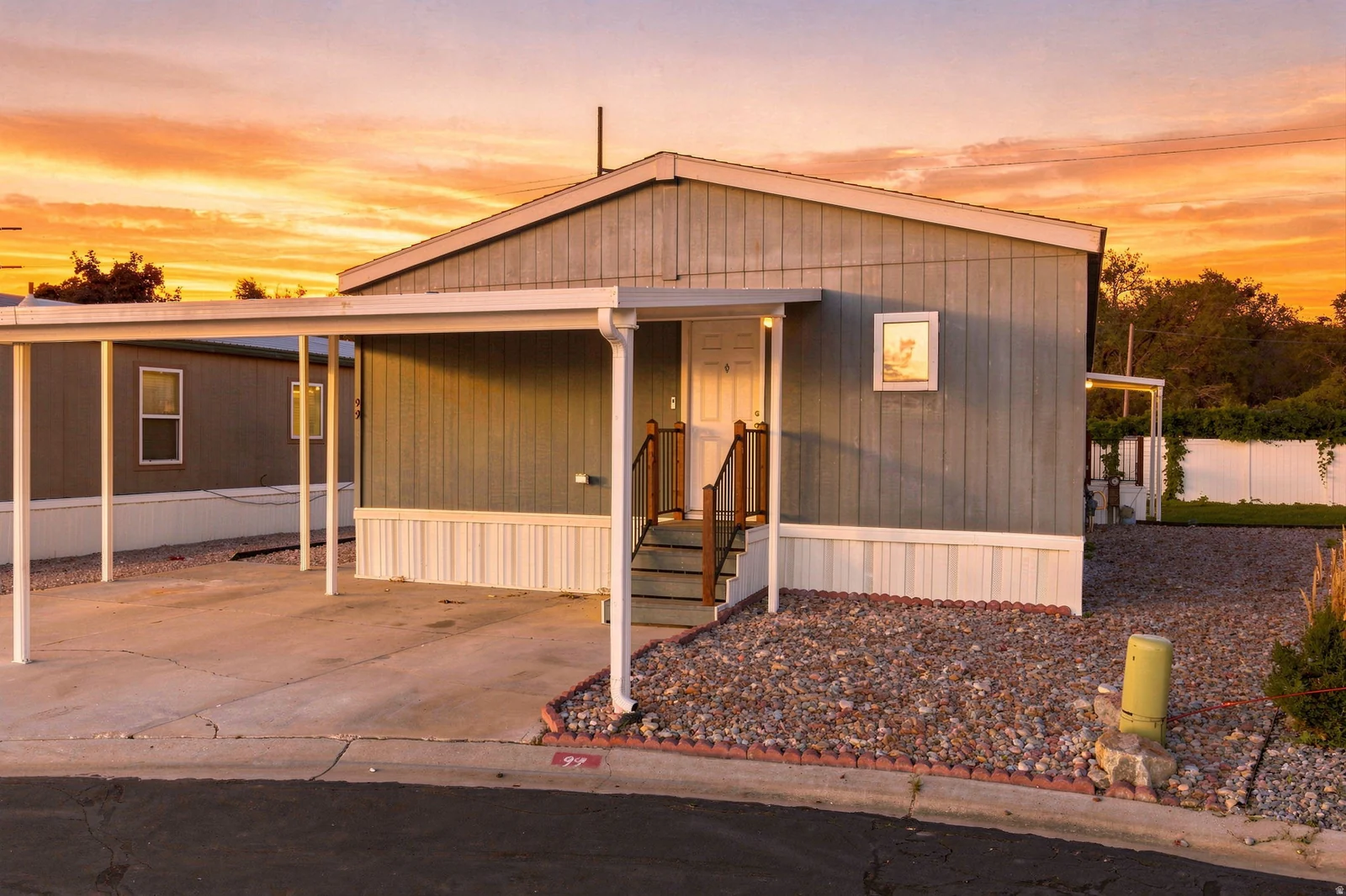 Exterior siding, covered carport, gravel landscaping, front entry porch with steps, and a white perimeter fence